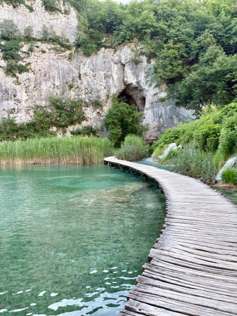 Une passerelle en bois au-dessus d'une eau turquoise, au pied d'une falaise