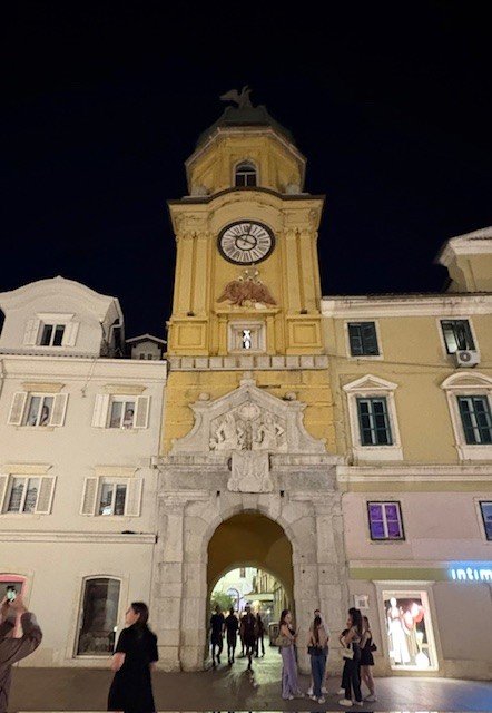 Une tour de l'horloge jaune avec une porte voûtée, illuminée le soir